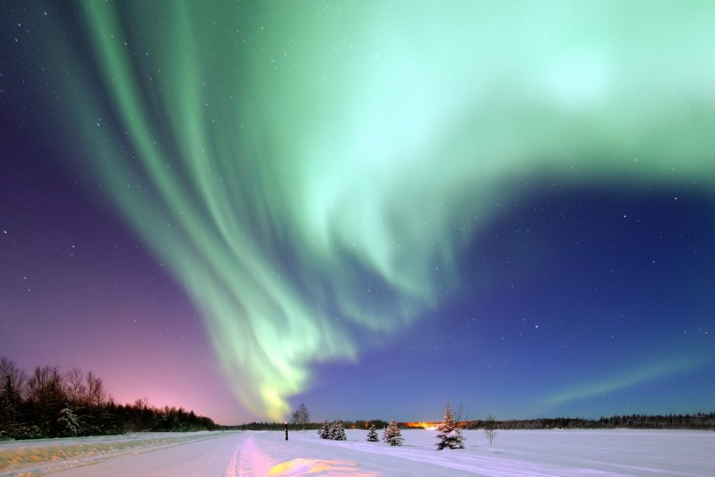 Aurora boreal iluminando el cielo sobre un paisaje nevado.