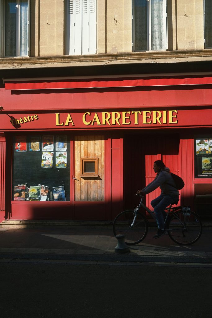Fachada de un teatro en La Provenza con ciclista pasando al atardecer.