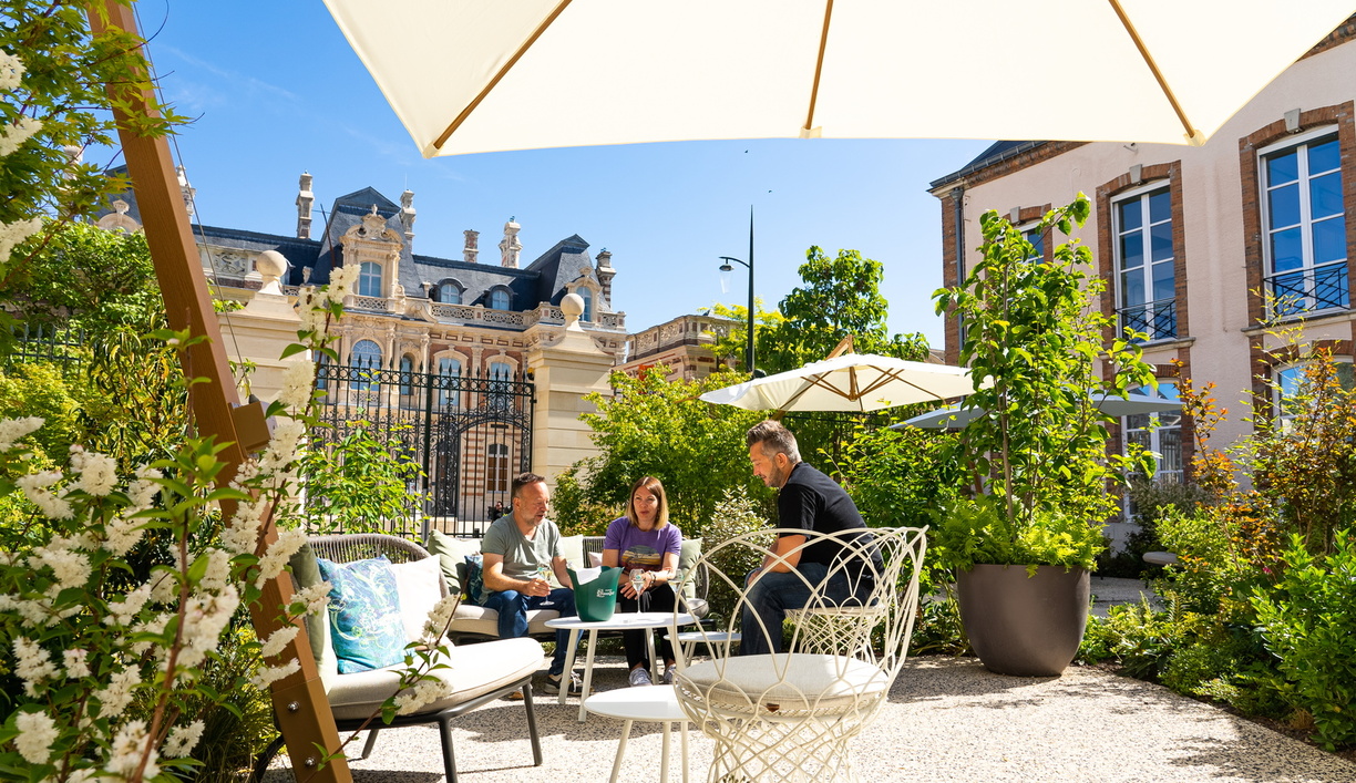 Turistas haciendo cata de vinos en el patio ajardinado de una mansion de champagne.