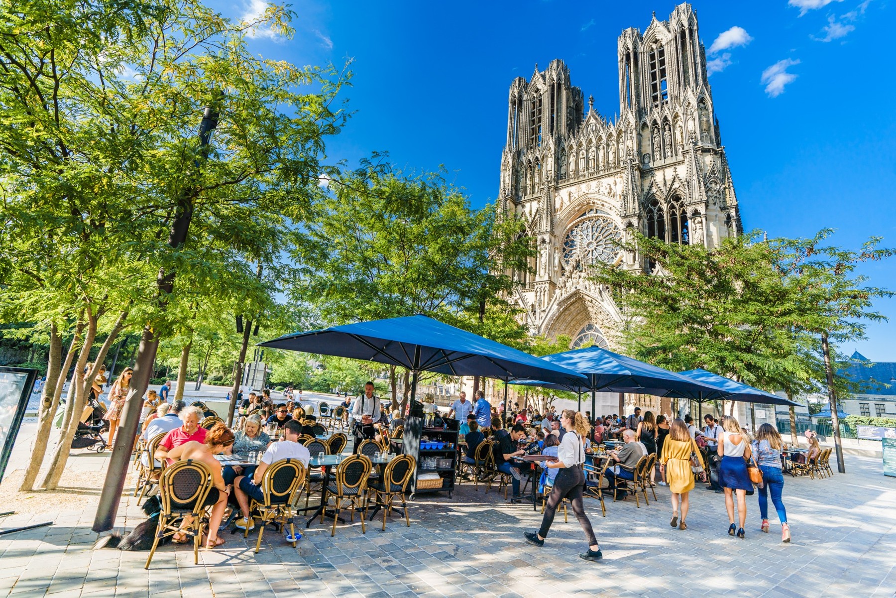 Terraza llena de turistas comiendo frente a la fachada de la Catedral de Reims en Francia